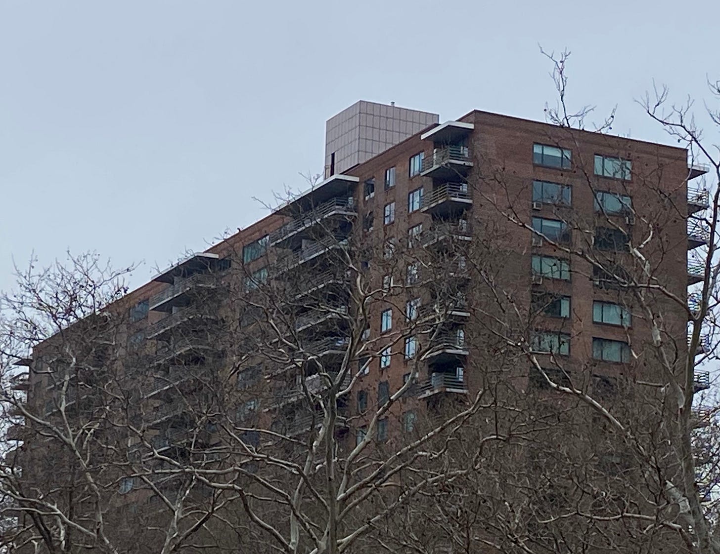 A brown rectangle of a building with wide windows and terraces. On the roof is a white box. A brown rectangle of a building with wide windows and terraces. On the roof is a white box.