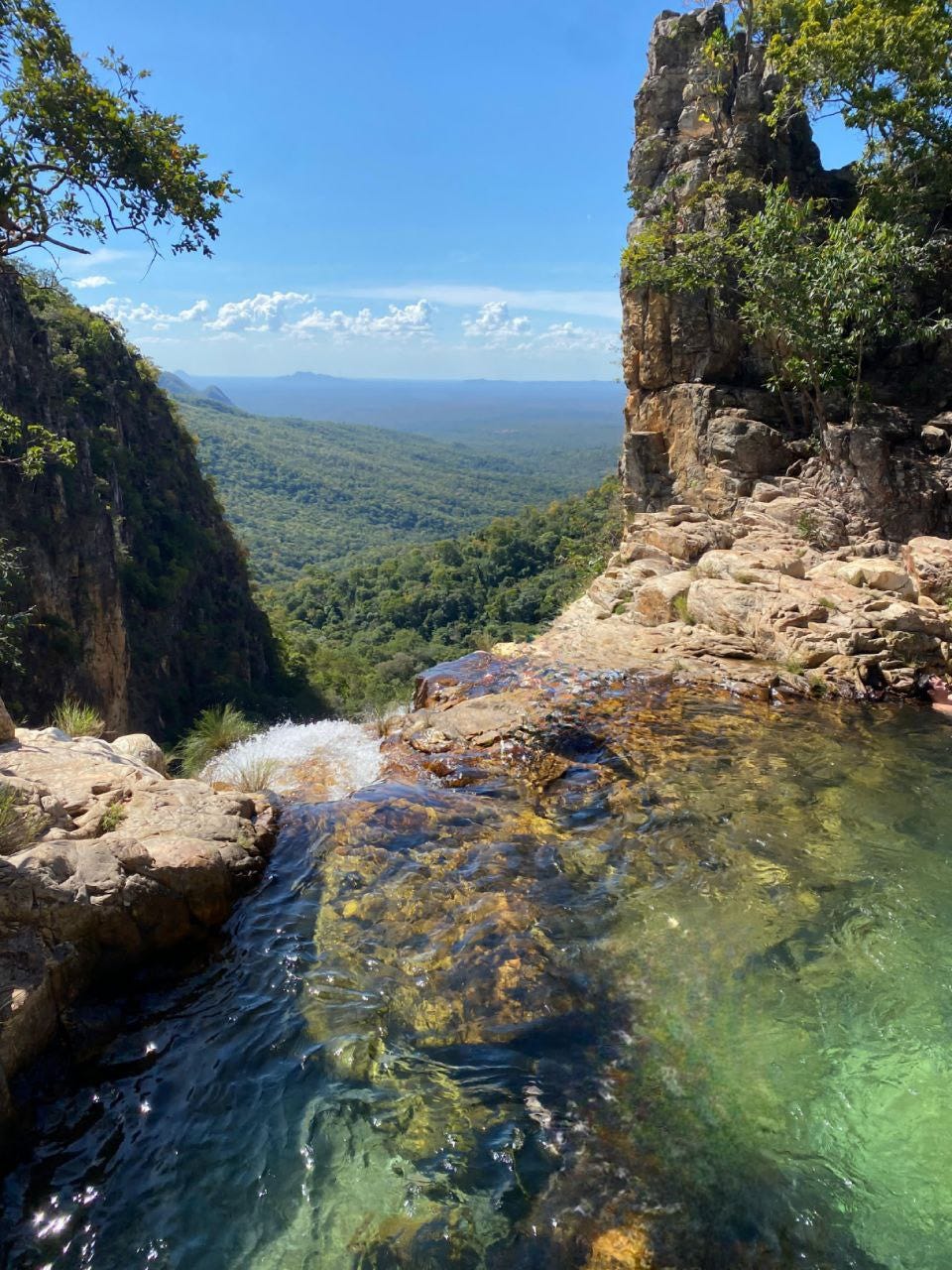 Pequeno poço para banho que deságua numa cachoeira, só vemos o topo mas ela está numa abertura na montanha e dá pra ver um vasto horizonte abaixo.