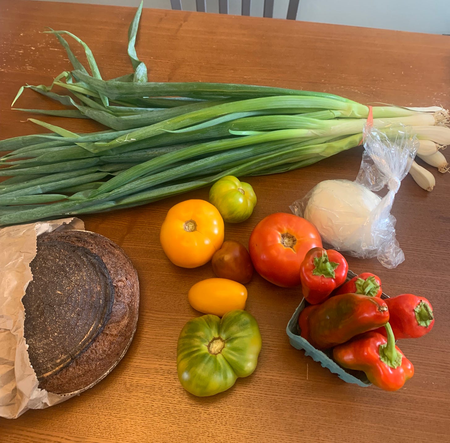 Several tomatoes, a loaf of bread, green onions and burrata