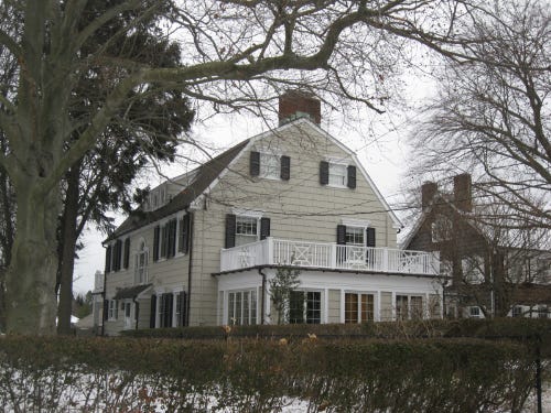 A white Dutch Colonial house behind a low hedge. A white Dutch Colonial house behind a low hedge.
