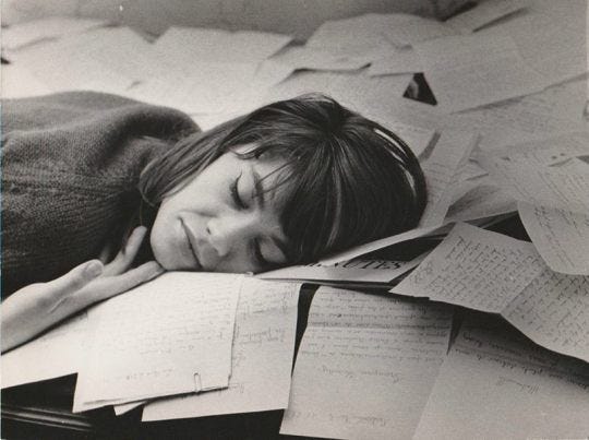 This may contain: a woman is sleeping on top of books and papers while she sleeps with her eyes closed