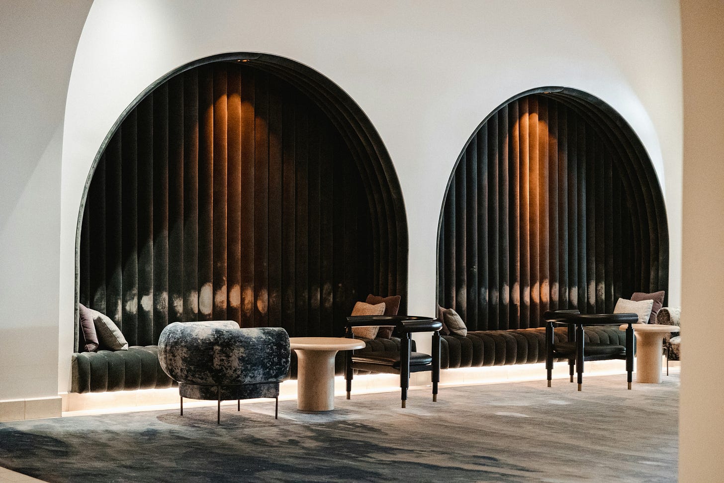 Arched lounge alcoves with curved seating, dark vertical paneling, and soft integrated lighting. Arched lounge alcoves with curved seating, dark vertical paneling, and soft integrated lighting.