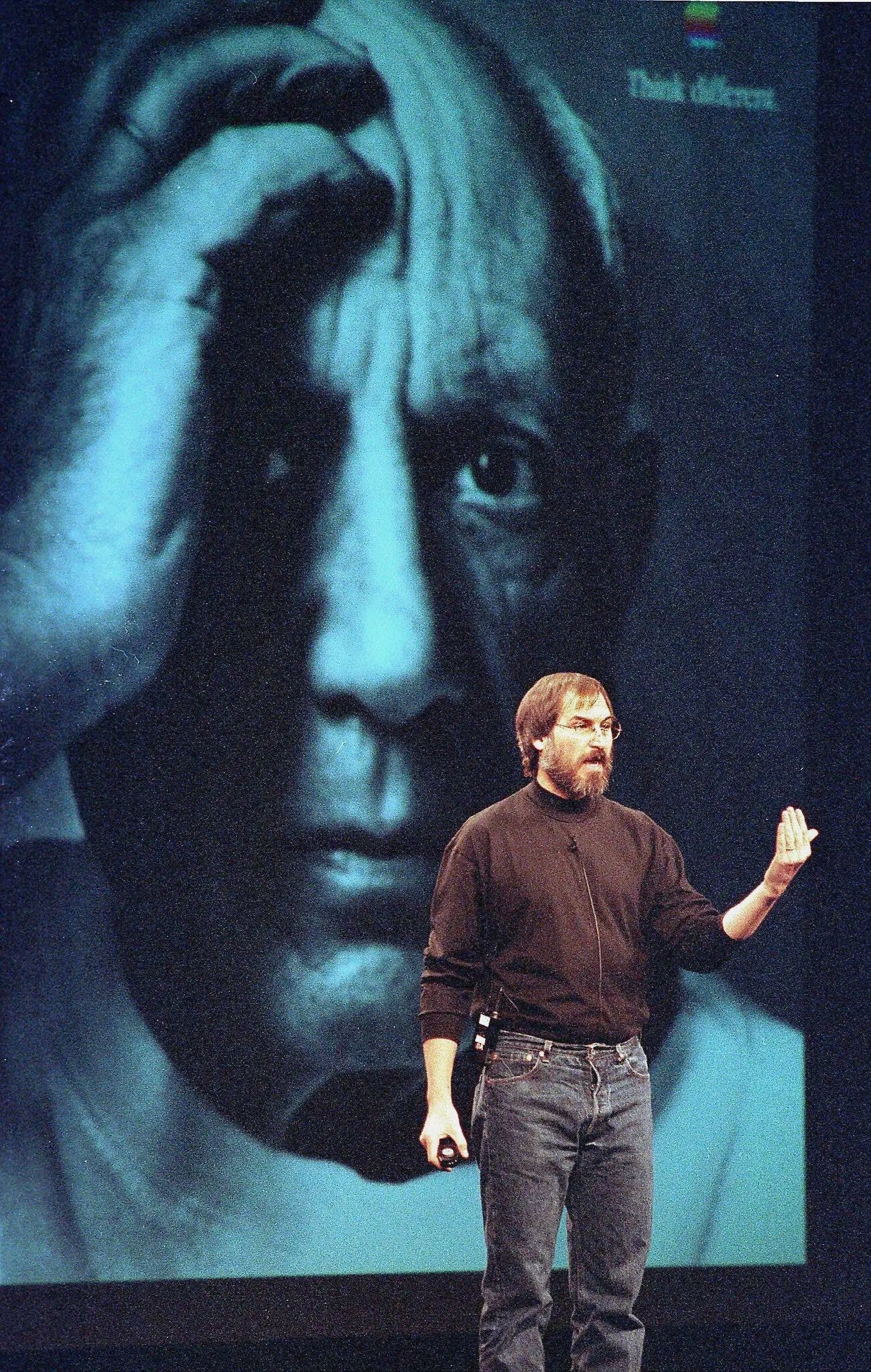 A person standing on stage with a person's face behind him

Description automatically generated