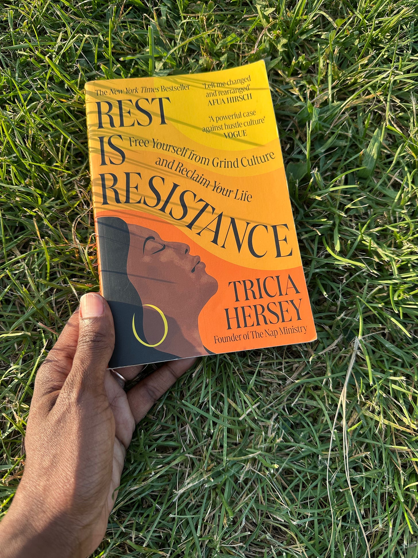 Rest Is Resistance by Tricia Hersey, held outdoors on green grass