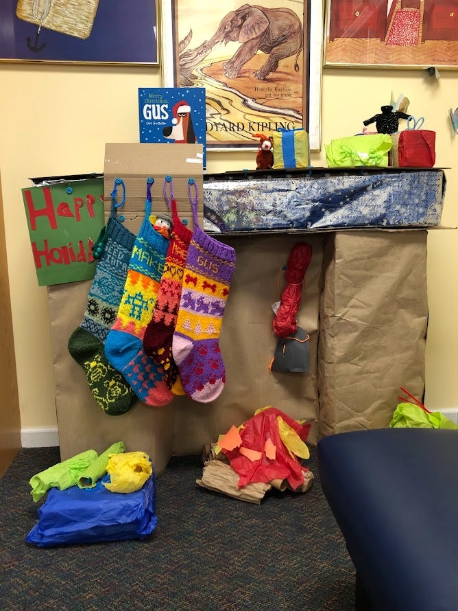 Cardboard fireplace mantle with four custom knit stockings.