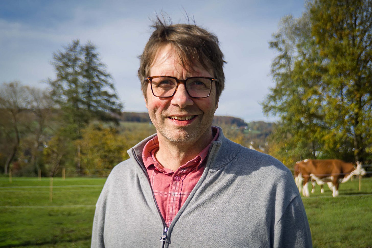 Florian Leiber, Leiter der Fachgruppe Nutztierwissenschaften am Forschungsinstitut für biologischen Landbau (FiBL), steht auf einer grünen Weide. Er trägt eine graue Jacke über einem roten Hemd und lächelt in die Kamera. Im Hintergrund sind herbstlich gefärbte Bäume, sanfte Hügel und eine braun-weisse Kuh zu sehen. Florian Leiber, Leiter der Fachgruppe Nutztierwissenschaften am Forschungsinstitut für biologischen Landbau (FiBL), steht auf einer grünen Weide. Er trägt eine graue Jacke über einem roten Hemd und lächelt in die Kamera. Im Hintergrund sind herbstlich gefärbte Bäume, sanfte Hügel und eine braun-weisse Kuh zu sehen.