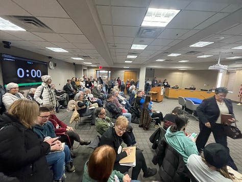 Photos of a packed meeting rooom filled with Carver County citizens testifying in opposition to renting jail cells to ICE