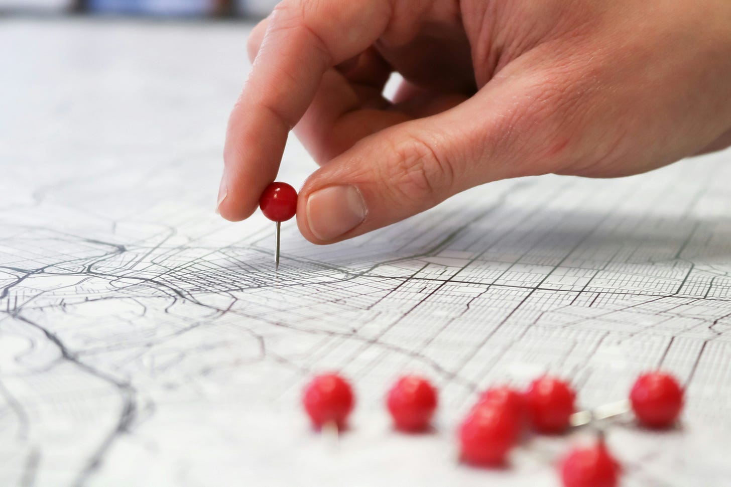 A hand is putting red pins into a map