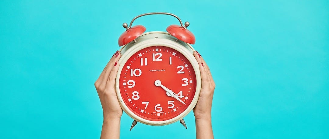 person holding red and beige twin bell analog alarm clock