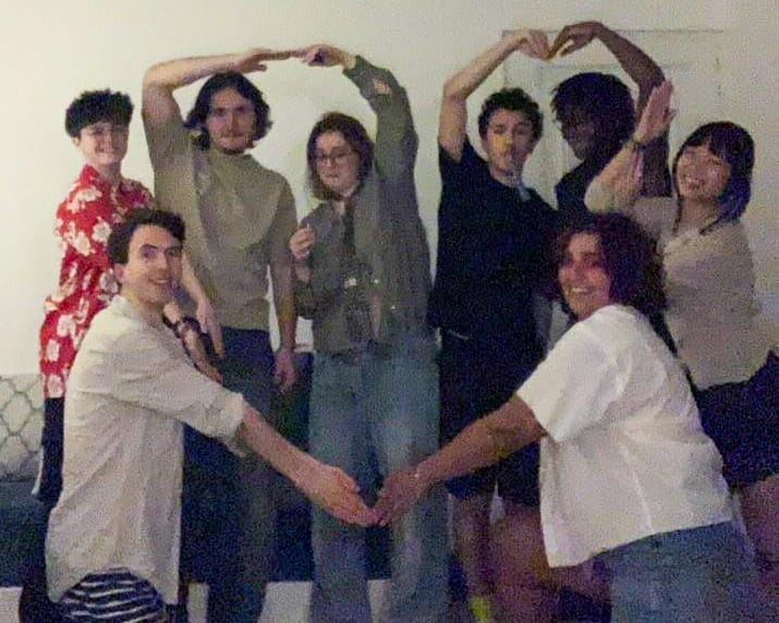 A friend group making a heart with their hands; Alex being mocked