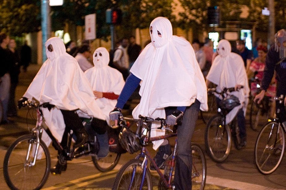 Image of cyclists wearing white capes at Halloween