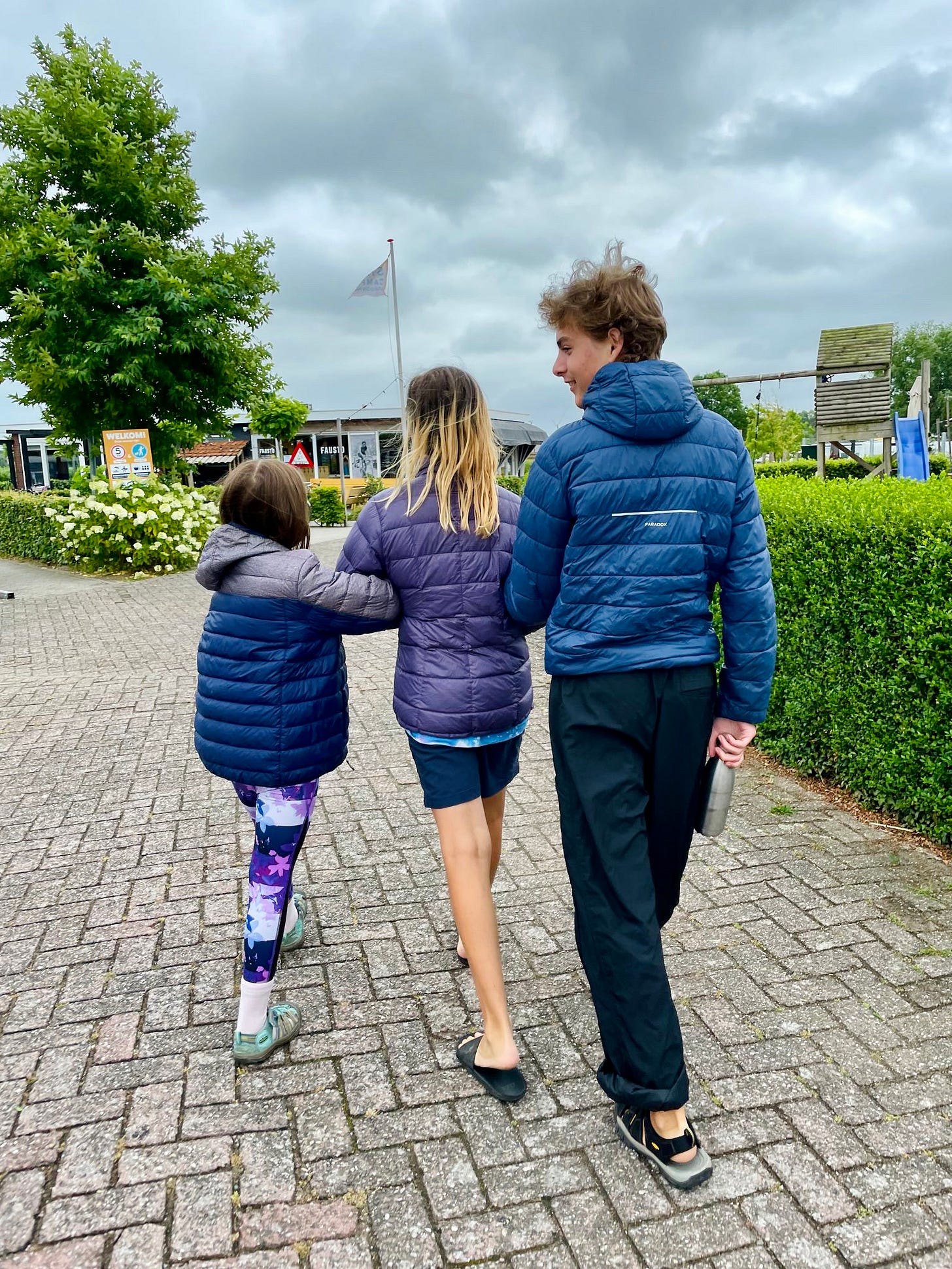 3 children facing away from camera, walking arm in arm.