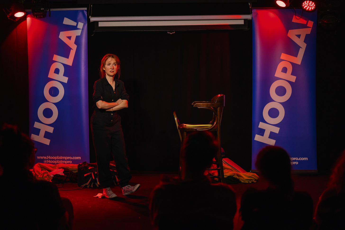 small ginger haired woman stands on stage looking worried, wearing a black jumpsuit
