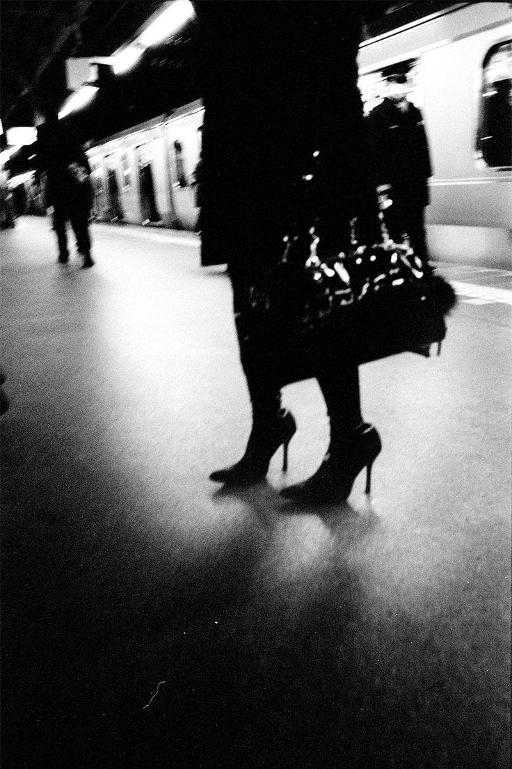 This may contain: black and white photograph of woman in high heeled shoes walking down the street at night This may contain: black and white photograph of woman in high heeled shoes walking down the street at night