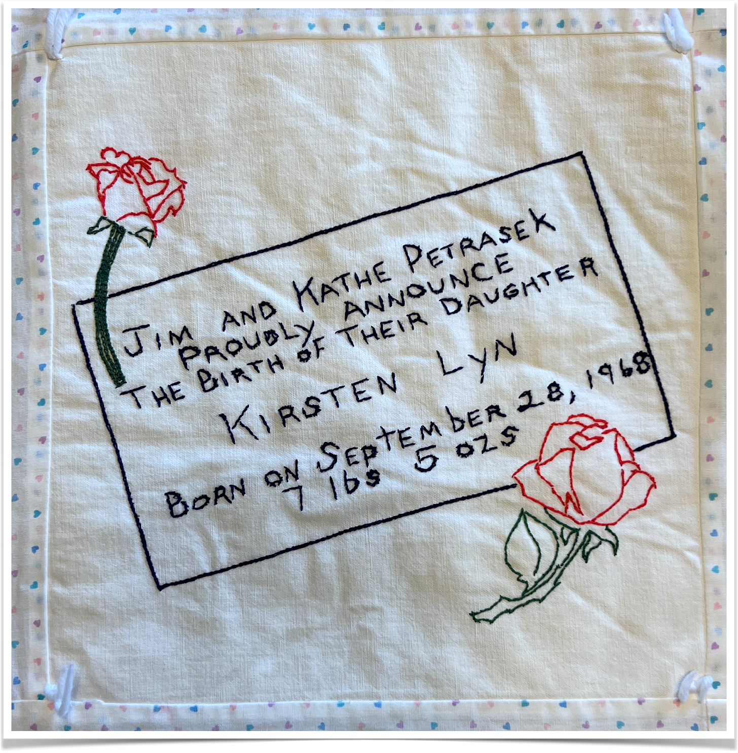 Black thread embroidering details of a birth certificate and featuring red roses.