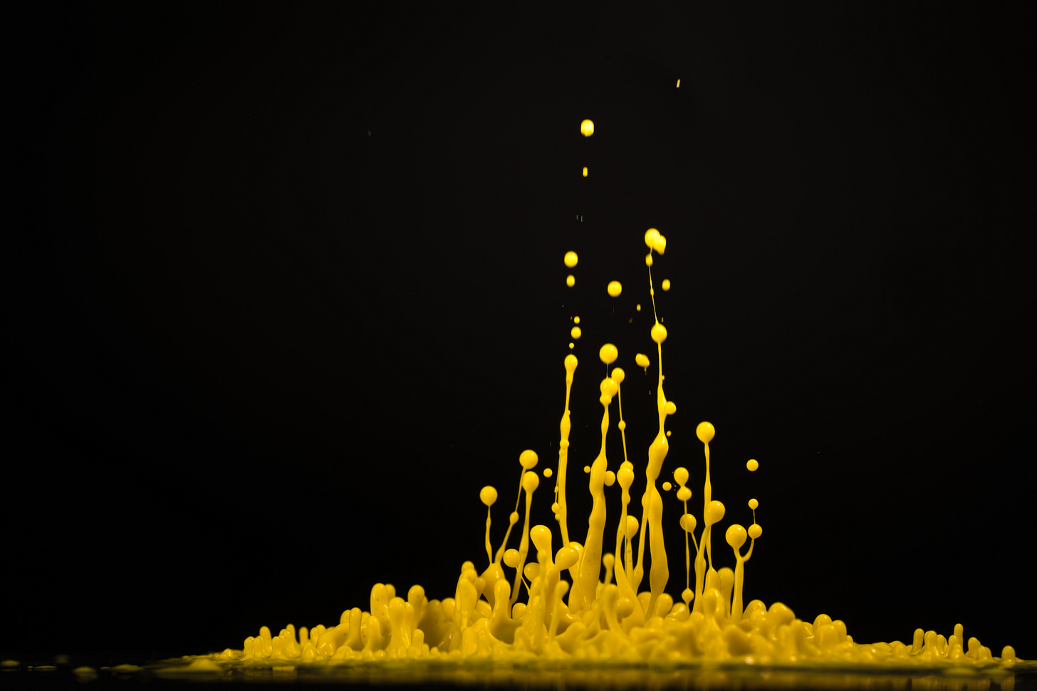 Yellow paint dripping upward, possibly a large dollop (to be precise) that was dropped  from above and photographed as it splashed