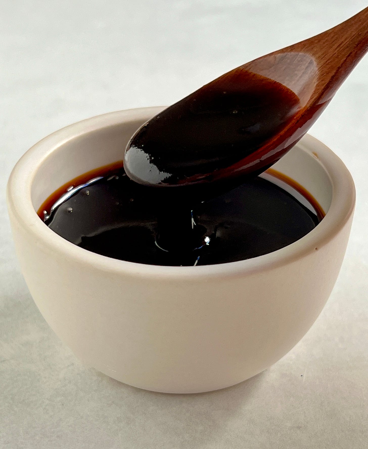 Close up of a wooden spoon with date syrup on it in an off white bowl.