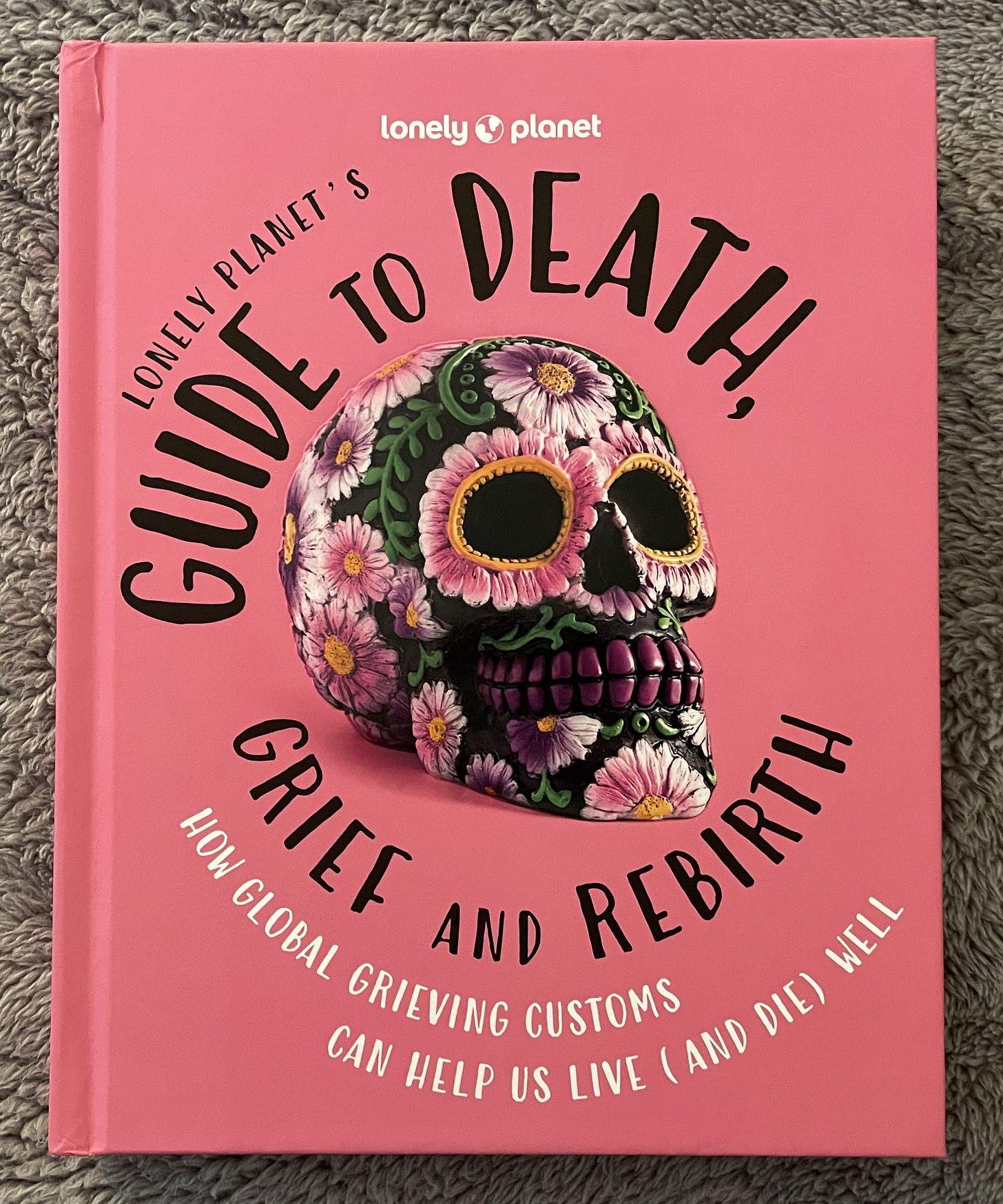 Bright pink book cover with large painted skull in center. The skull is black and decorated with pink flowers wtih gold centers.
