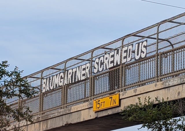 Overpass sign reads: Baumgartner Screwed Us