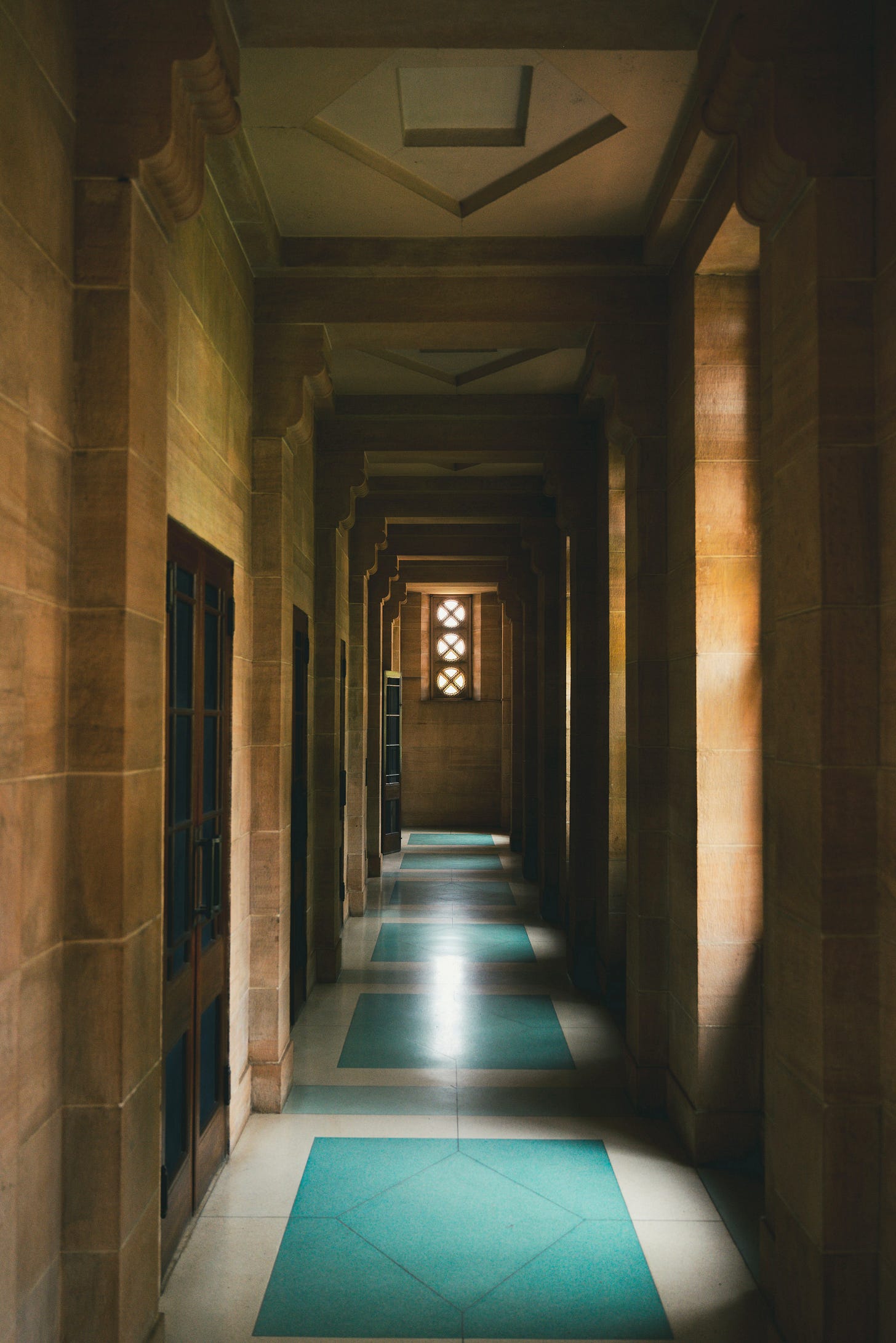 A long stone corridor framed by repeating columns and warm natural light. A turquoise geometric pathway guides movement through the space, creating a strong sense of orientation, visual clarity, and ease of navigation. A long stone corridor framed by repeating columns and warm natural light. A turquoise geometric pathway guides movement through the space, creating a strong sense of orientation, visual clarity, and ease of navigation.