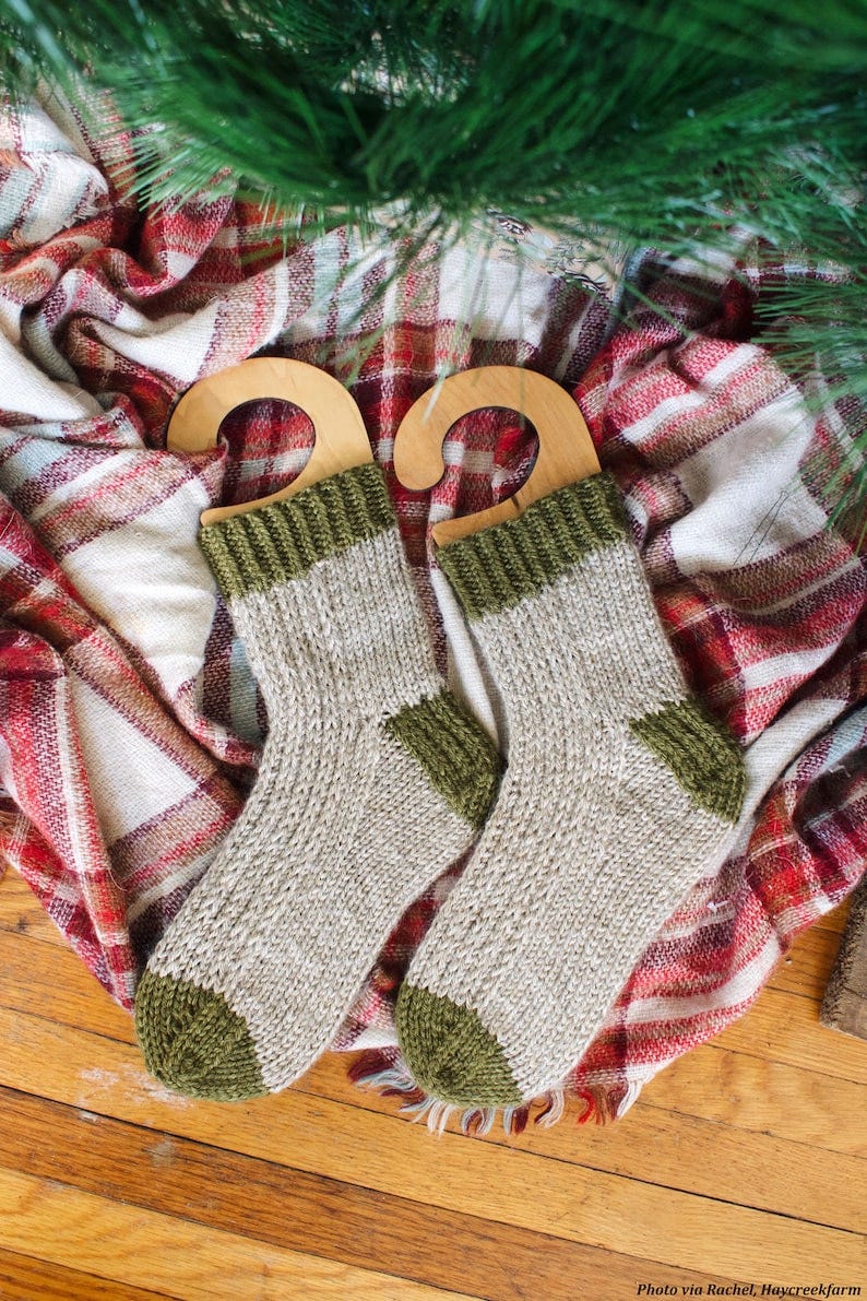 May include: Two pairs of knitted socks with green and beige stripes. The socks are hanging on wooden hangers. The socks are on a plaid blanket.