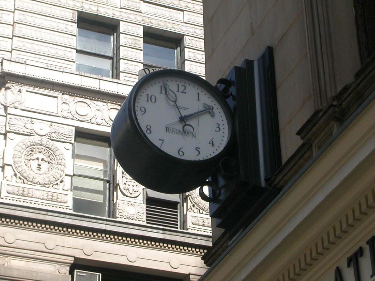 A black cast-iron street clock mounted on the corner of a building at Broadway and 22nd Street in Manhattan, its white face reading 1:56 — the exact stopped time referenced in TMBG's "Four Of Two."