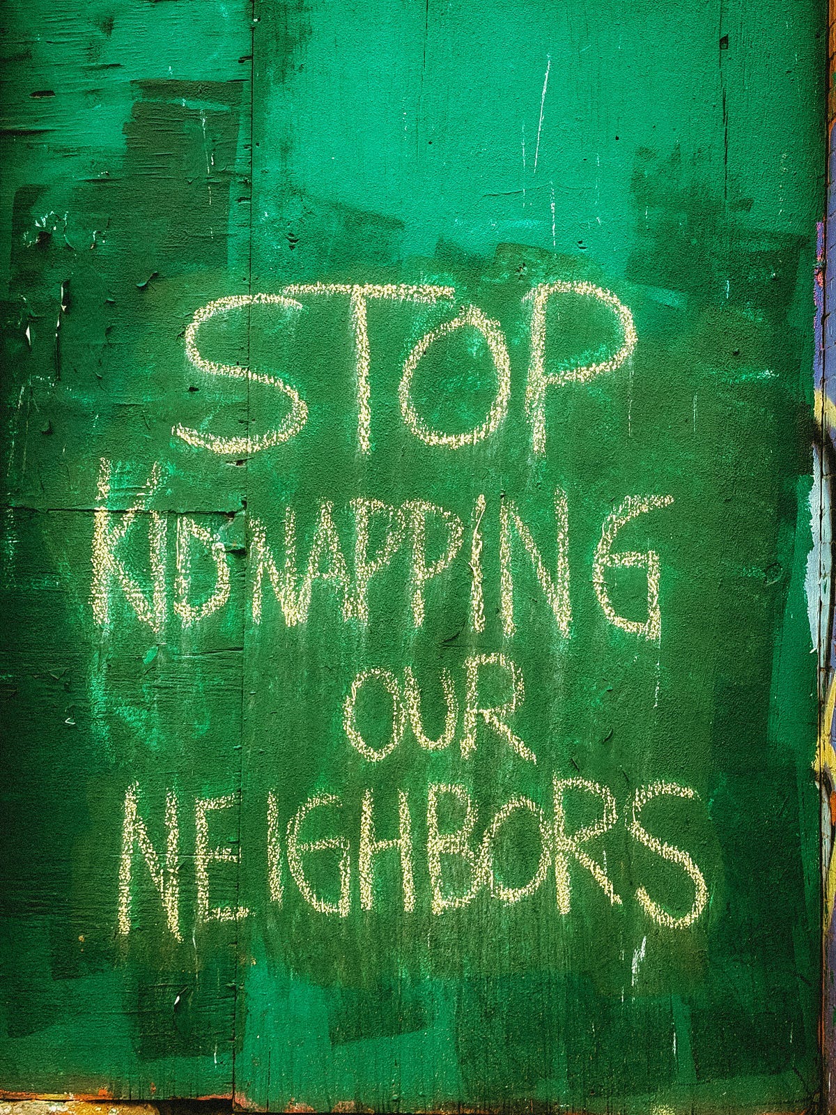 “Stop Kidnapping Our Neighbors” written in chalk on a green washed wall “Stop Kidnapping Our Neighbors” written in chalk on a green washed wall