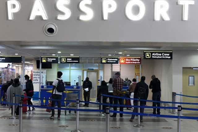 Interior of building with people standing in queues and a large sign saying "passport" Interior of building with people standing in queues and a large sign saying "passport"
