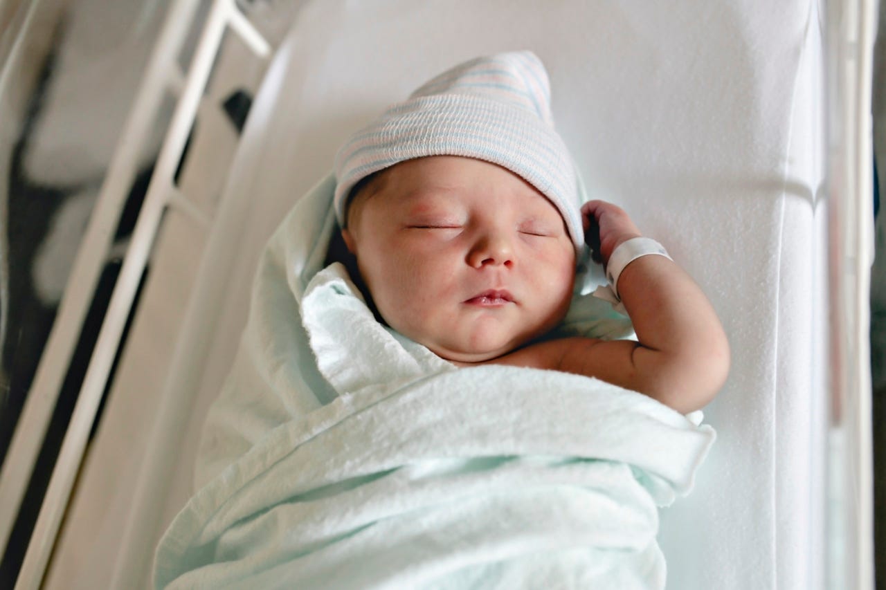 A Newborn baby asleep, swaddled in hospital blanket and wearing a hat