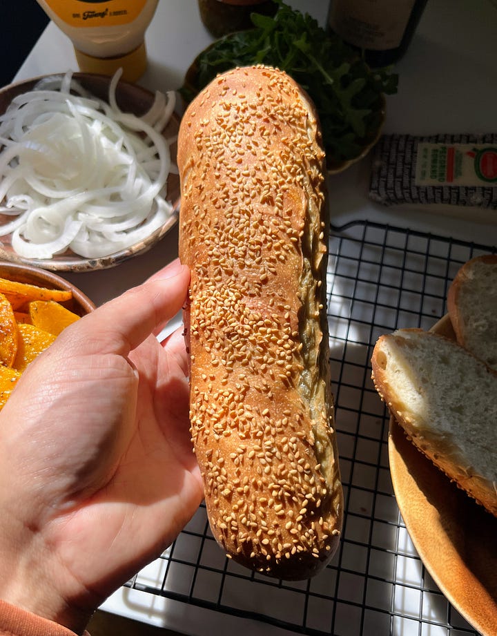 Hand holding hoagie roll, sandwich being assembled