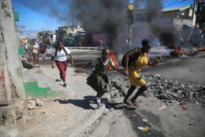 FILE - A woman and her daughter run past a barricade that was set up by police protesting bad police governance in Port-au-Prince, Haiti, Jan. 26, 2023. Haiti's latest crisis entered full throttle following the 2021 assassination of President Jovenel Moïse, when current Prime Minister Ariel Henry emerged in a power struggle as the country’s leader and the country's nearly 200 gangs have taken advantage of the chaos, warring for control. (AP Photo/Odelyn Joseph, File)