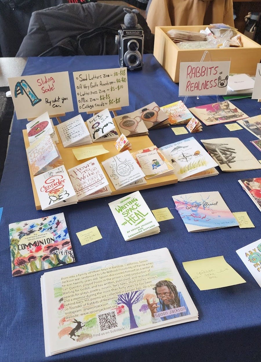 Picture of many zines laid out on a table with a blue tablecloth.