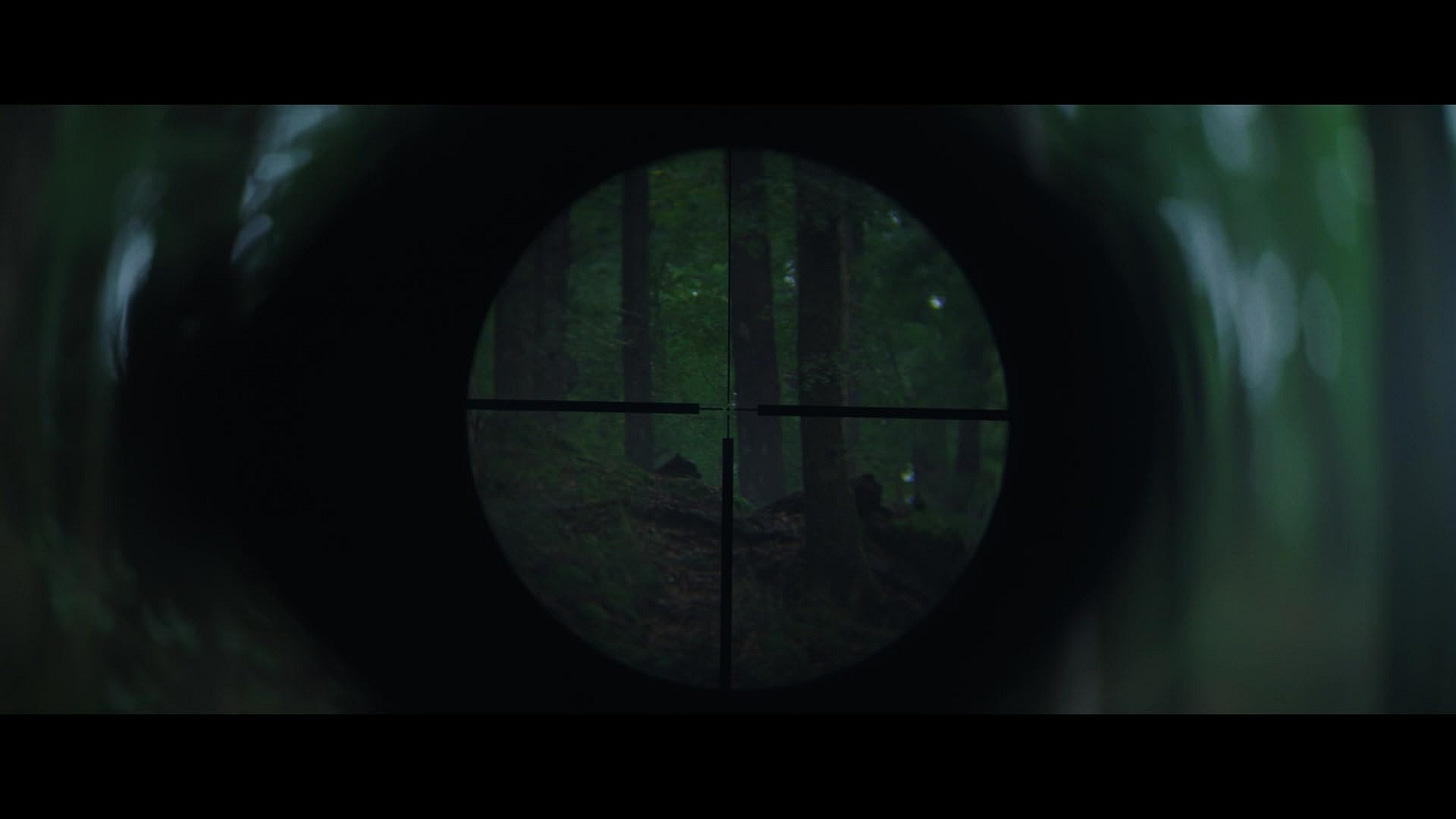 Wolf Man sniper scope view — First-person view through a rifle scope aimed at a shadowy figure moving in a foggy forest.