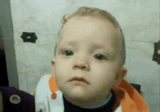 a baby is making a sad face in front of a wall . a baby is making a sad face in front of a wall .