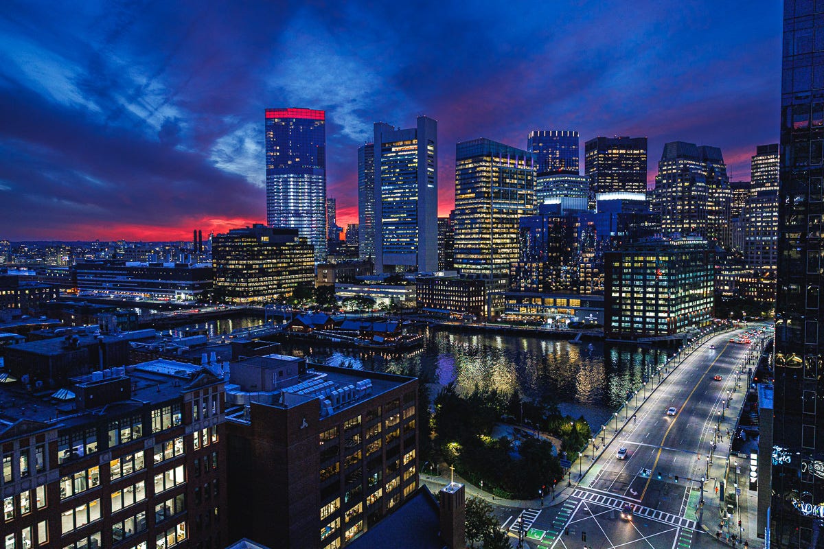 Panoramic Boston Seaport skyline at blue hour with glowing reflections on Fort Point Channel.