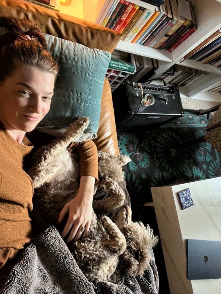 Linea laying on a couch with a weighted blanket and her dog who is upside down with its feet sticking toward her face.