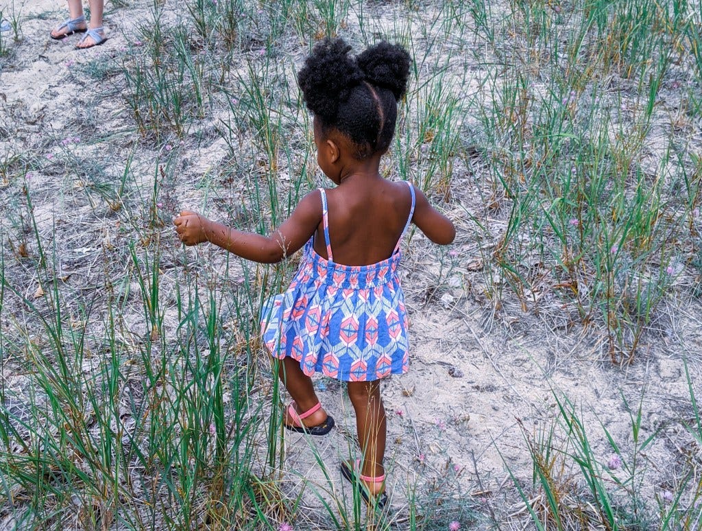 A young child in a colorful dress walks through grassy terrain, embodying a sense of joy and exploration.