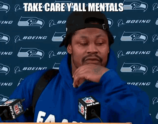 a man wearing a seahawks sweatshirt stands in front of a boeing banner