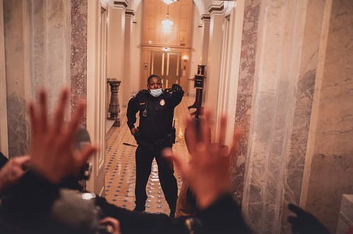 A U.S. Capitol police officer stands in a hallway blocking a crowd in the foreground from entering.