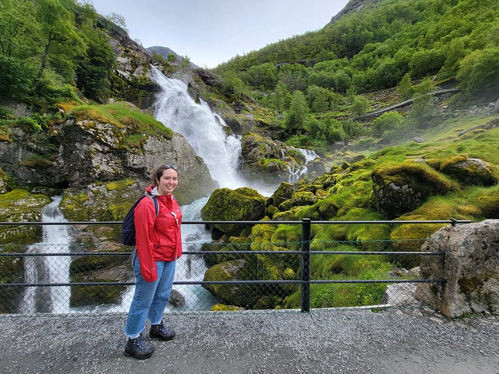 Four pictures of Shira in red coats: one raincoat (in front of a waterfall), one red trench in the sun, one winter coat in the snow, and the same red trench but this time with matching sunglasses.