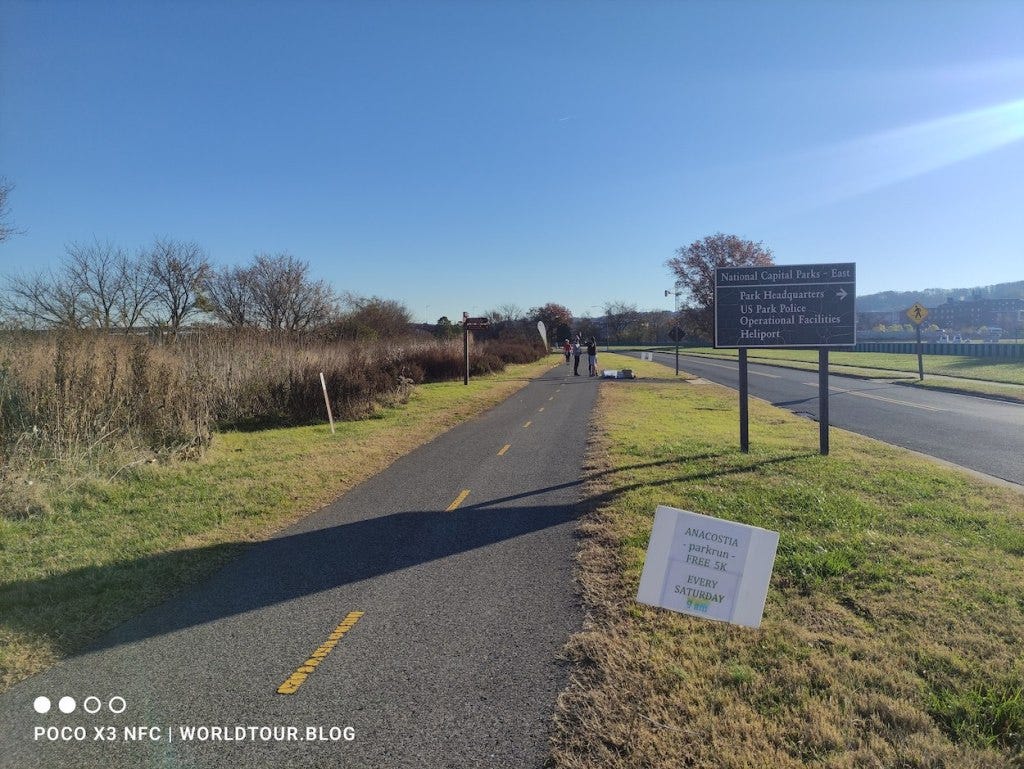 A sign advertises the parkrun as volunteers complete the simple setup next to a sign pointing to National Capital Parks - East, park HQ.