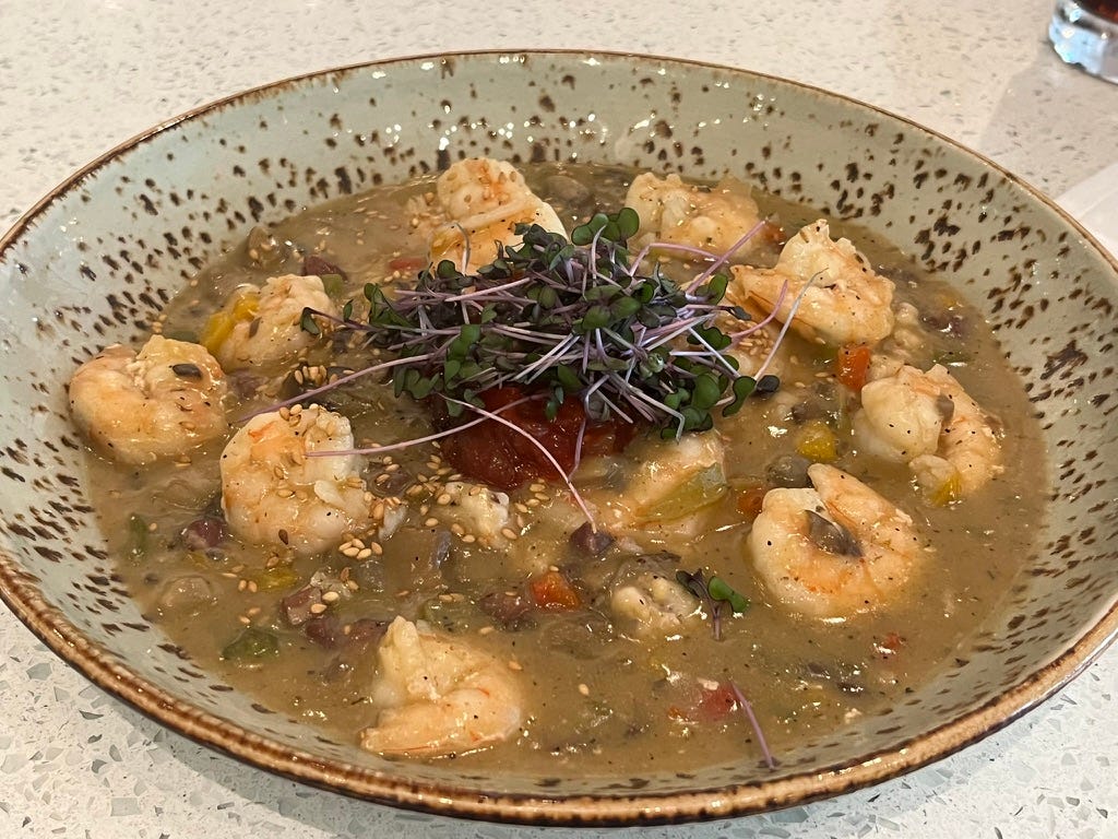 About a dozen shrimp on grits with light brown broth, and garnished with green sprouts and a red condiment