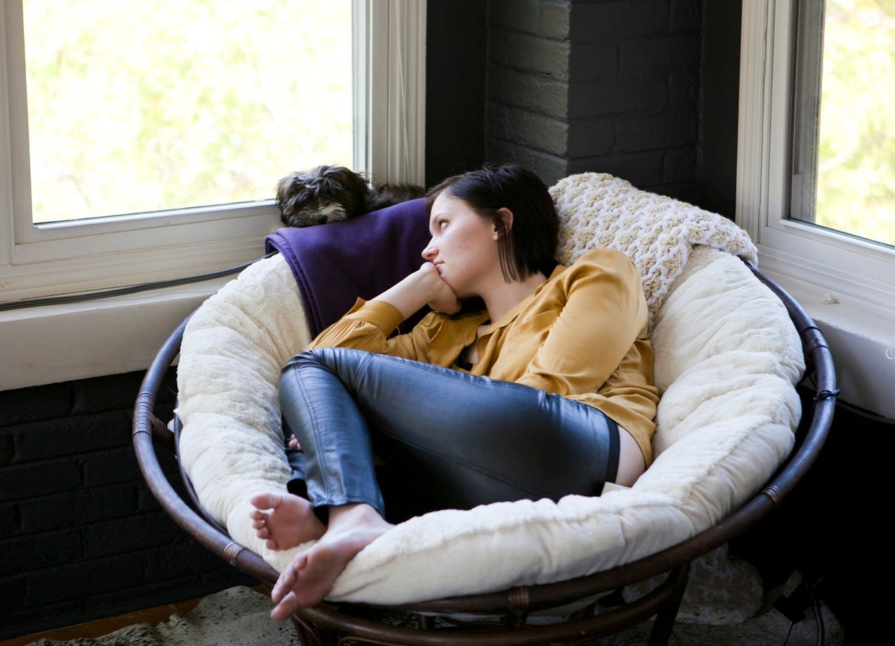 a picture of a woman (me) curled up in a papasan chair with a fluffy gray dog on the windowsill behind me