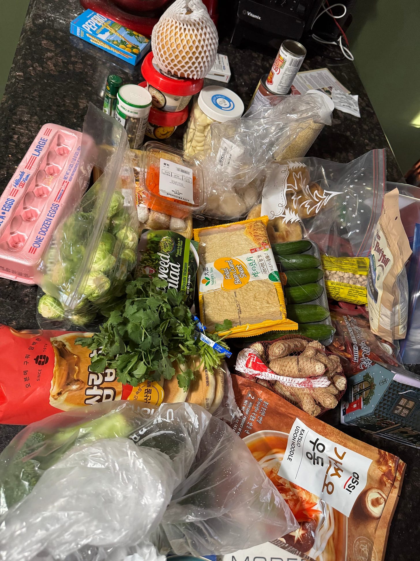 Counter full of groceries included several green vegetables, noodle meal kit, and eggs
