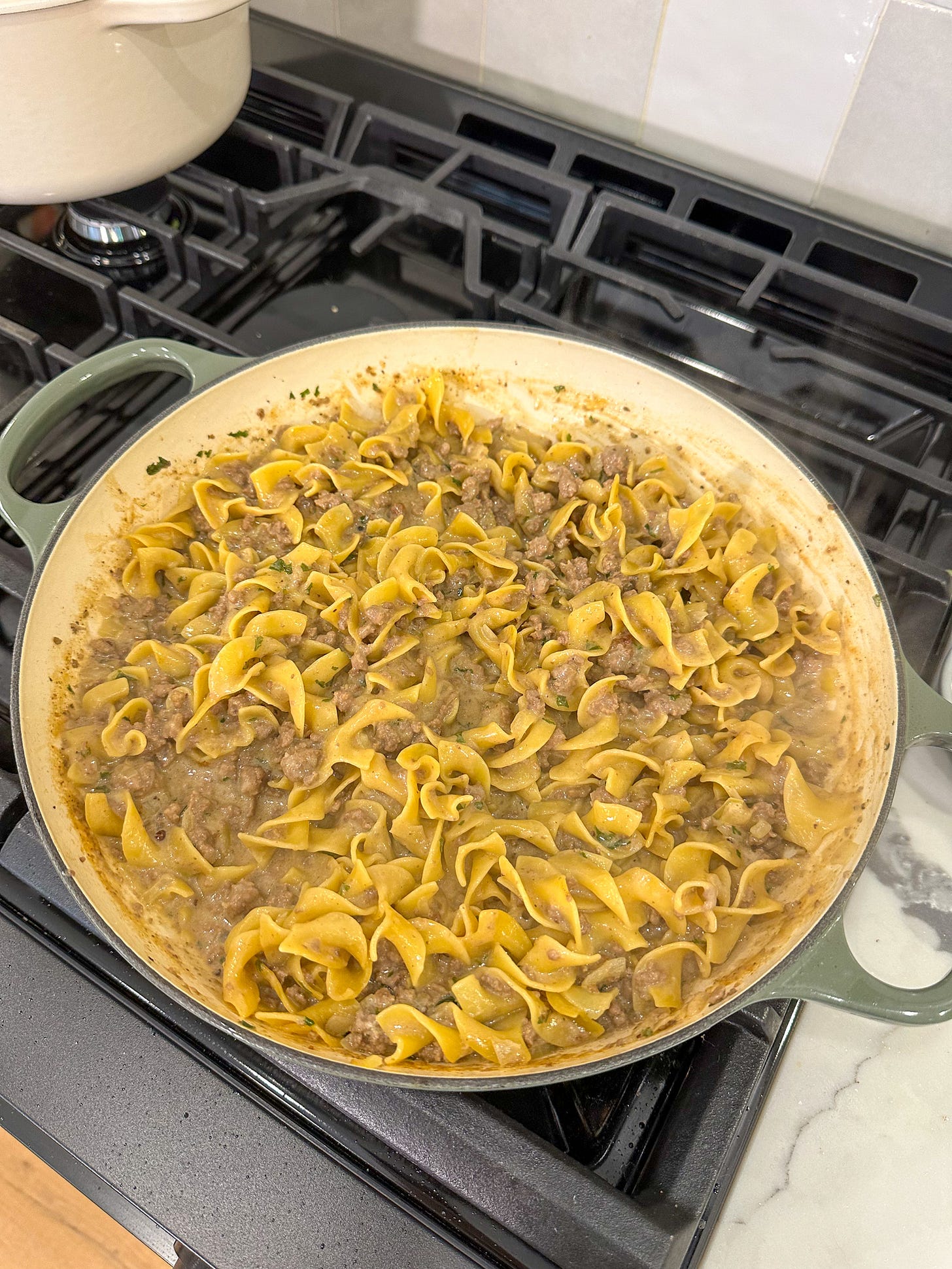 One pot beef stroganoff simmering in a braiser on the stovetop.