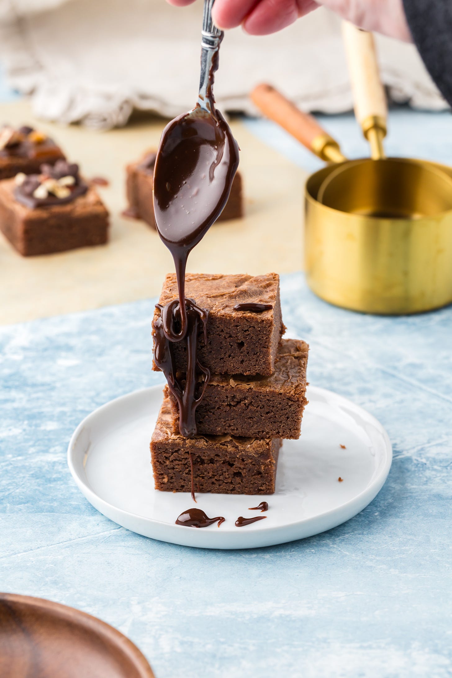 a stack of brownies with chocolate drizzle being poured over the top. 
