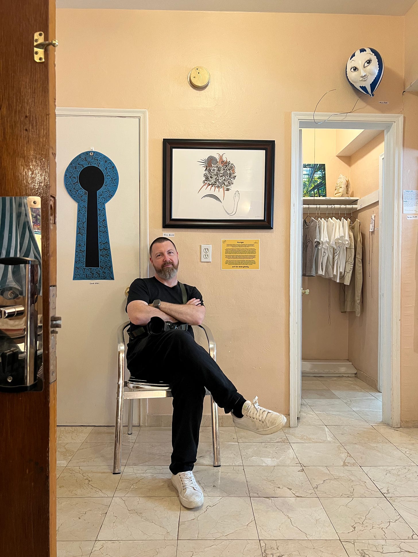 A man sitting on a chair with art work on the walls, doors and in the closet