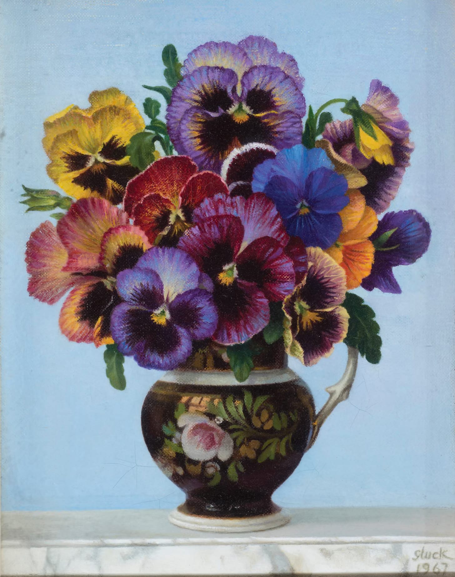 A painting of a vibrant bouquet of pansies, in shades of purple, red, yellow, blue, pink, and orange, arranged in a decorative floral dark vase against a light blue background. The vase is sitting on top of a marble table. There are dark green leaves surrounding the flowers. Gluck's signature and the year are in the bottom right corner in white. A painting of a vibrant bouquet of pansies, in shades of purple, red, yellow, blue, pink, and orange, arranged in a decorative floral dark vase against a light blue background. The vase is sitting on top of a marble table. There are dark green leaves surrounding the flowers. Gluck's signature and the year are in the bottom right corner in white.