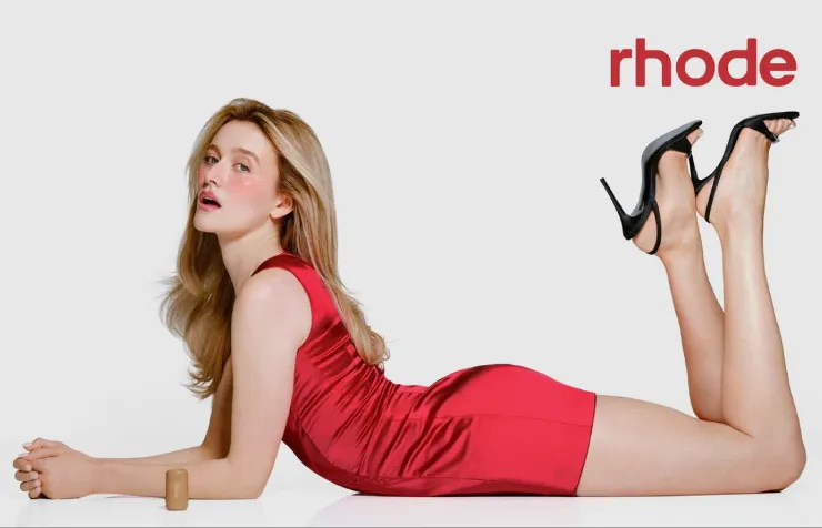 Actress Sarah Pidgeon lying on a white background in a red satin mini dress for the Rhode Spring 2026 campaign launch.