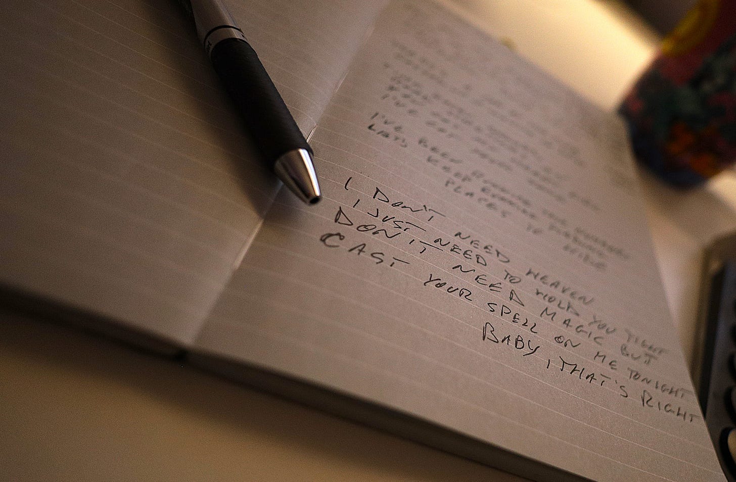 An image of a pen across part of the page of my songwriting journal, with lyrics written on it.